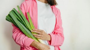 A woman in a pink jacket holding fresh spring onions against a white background.