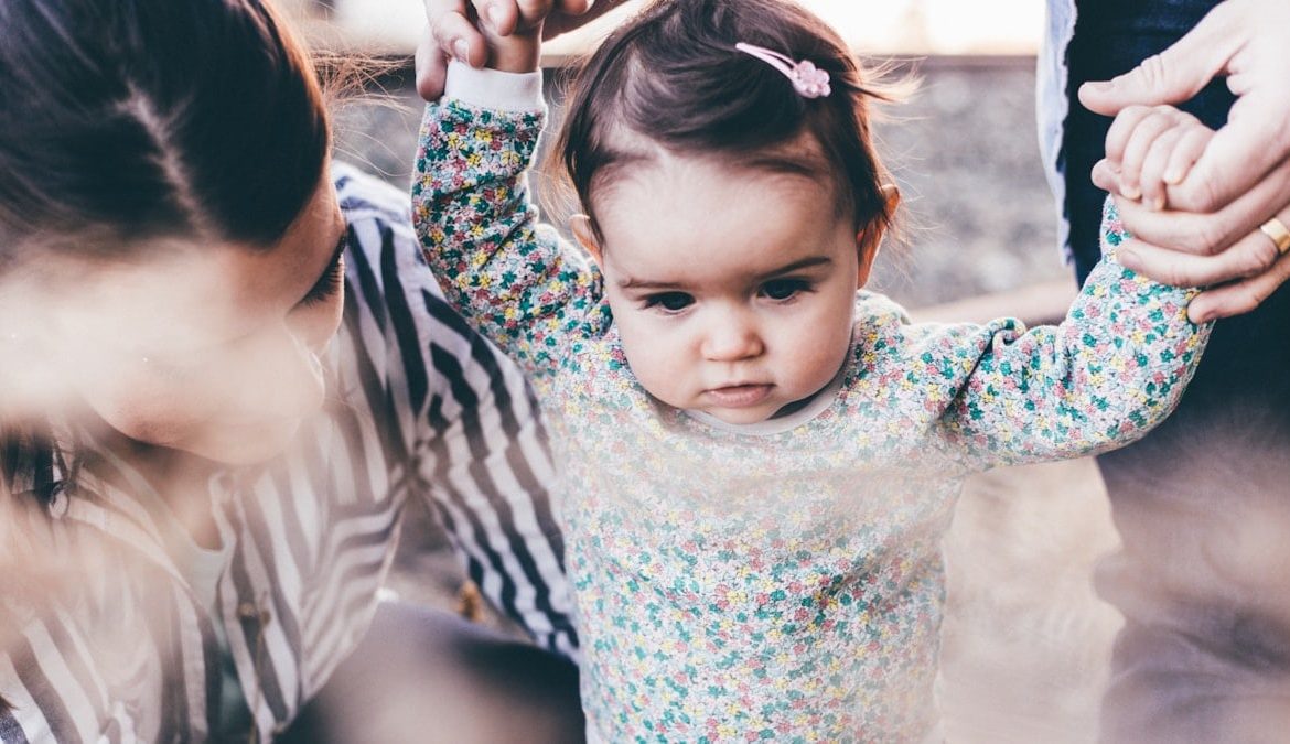 woman holding girl while learning to walk taken at daytime