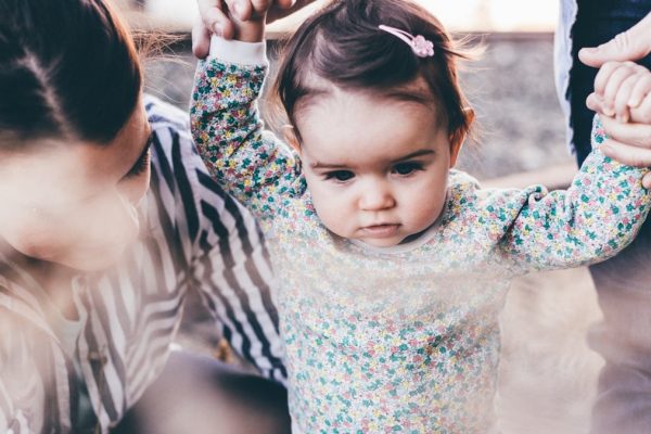 woman holding girl while learning to walk taken at daytime