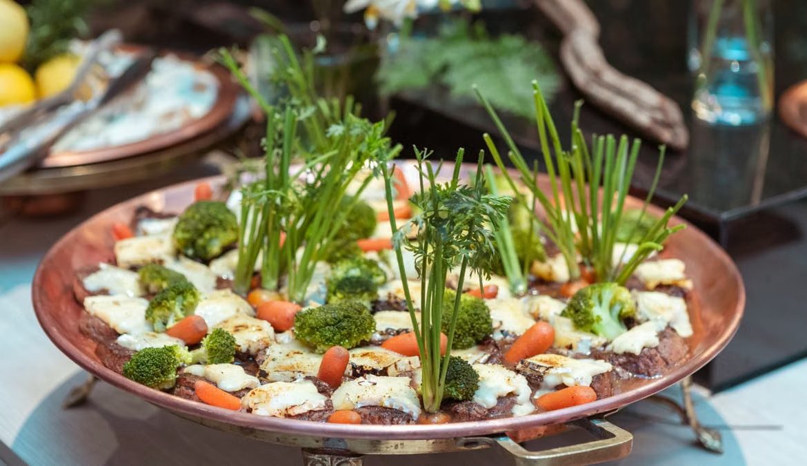 An artistic presentation of vegetables including broccoli, carrots, and greens on a copper platter.
