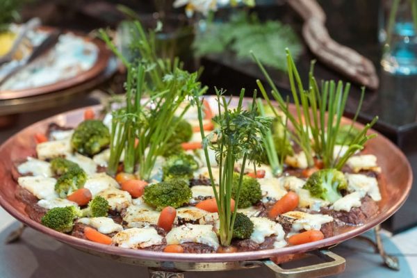 An artistic presentation of vegetables including broccoli, carrots, and greens on a copper platter.