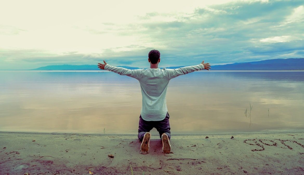 man wearing gray long-sleeved shirt beside seashore during daytime